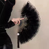 A hand points to the golden edge of a vintage lace-trimmed folding fan with a black feather trim.