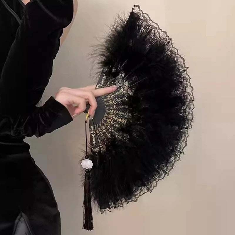A hand points to the golden edge of a vintage lace-trimmed folding fan with a black feather trim.