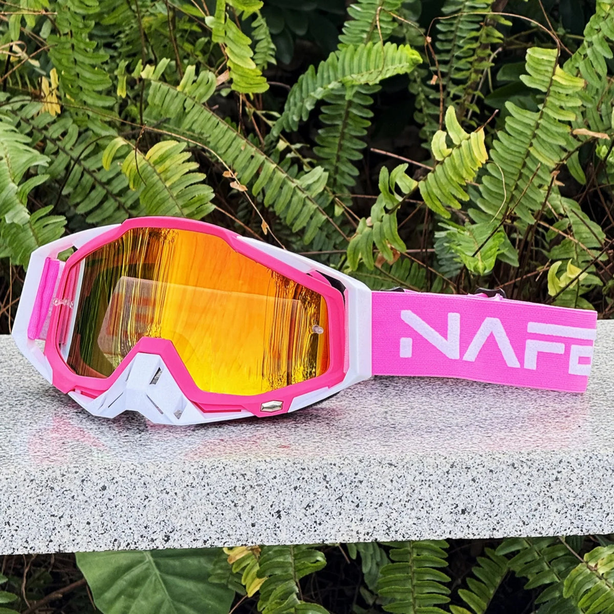 Pink and white HD Motocross goggles with an orange anti-fog lens resting on a gray surface.