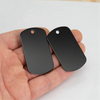 Two black aluminum dog tags are held in a person's hand against a white background.