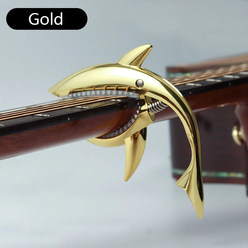 Gold shark-design guitar capo with zinc alloy build shown on a wooden guitar neck.