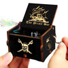 A dark wooden music box with a pirate theme and a skull design is being held by a hand.