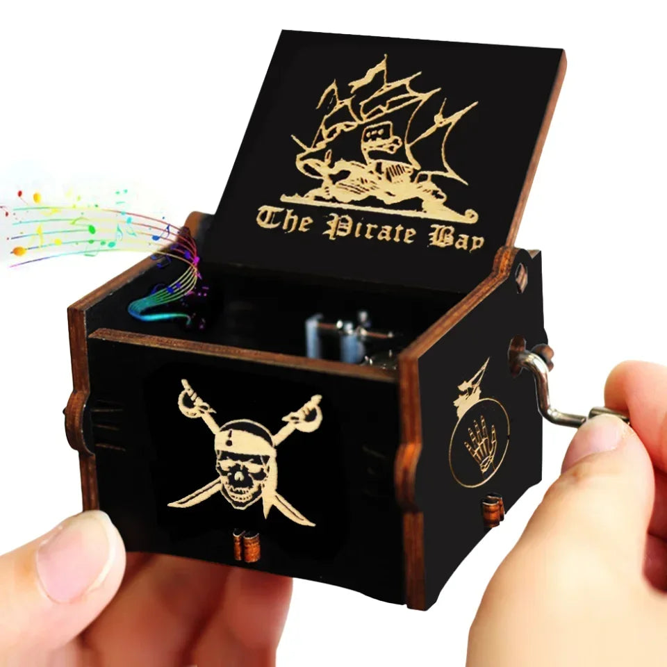 A dark wooden music box with a pirate theme and a skull design is being held by a hand.