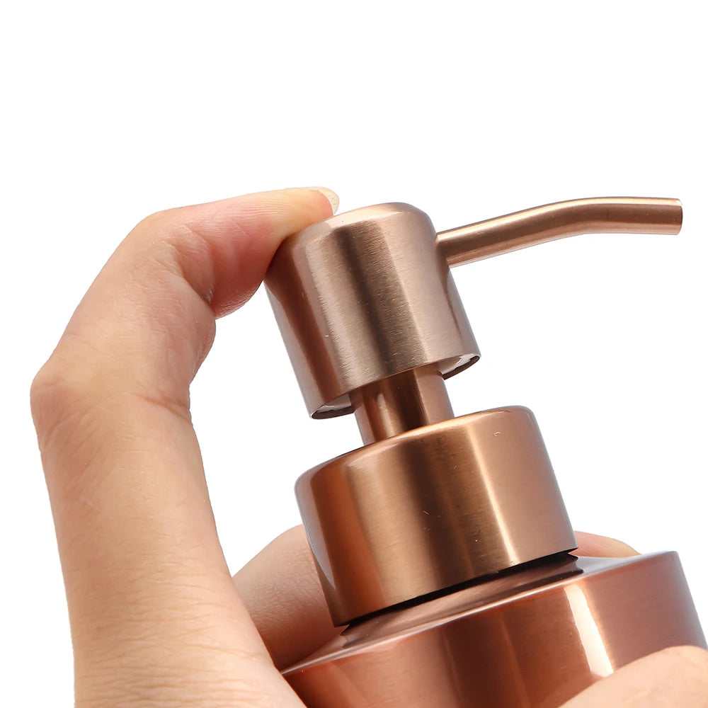 A hand is holding a rose gold stainless steel liquid soap dispenser pump bottle.