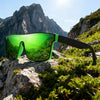 A pair of bright green sports sunglasses resting on a rocky outdoor landscape with mountains in the background.