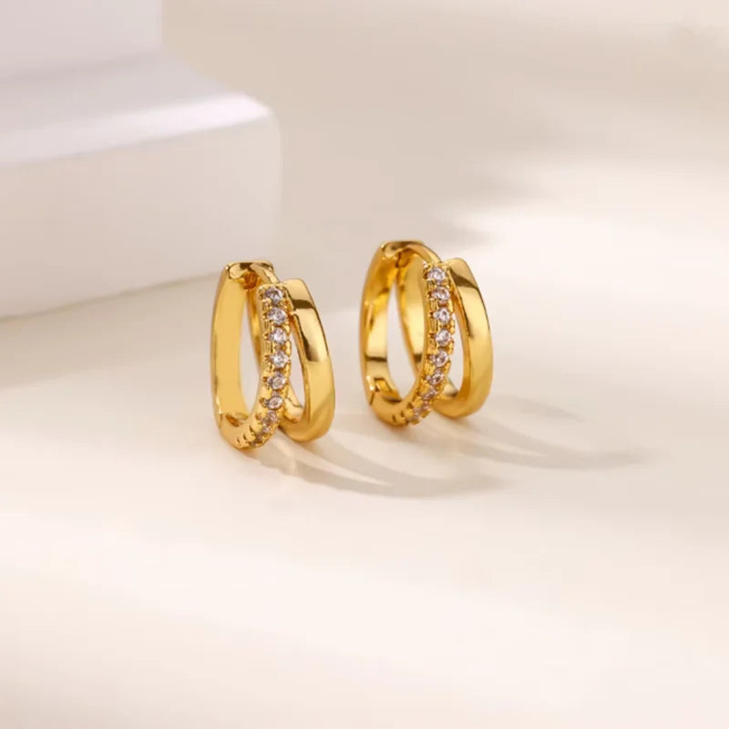 Pendientes de aro dorados adornados con piedras de circonita cúbica brillante, exhibidos sobre una superficie clara.