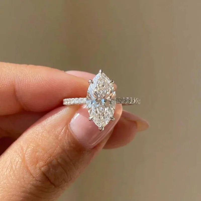 Une main tient une bague en argent sterling avec zircon marquise et bande pave.