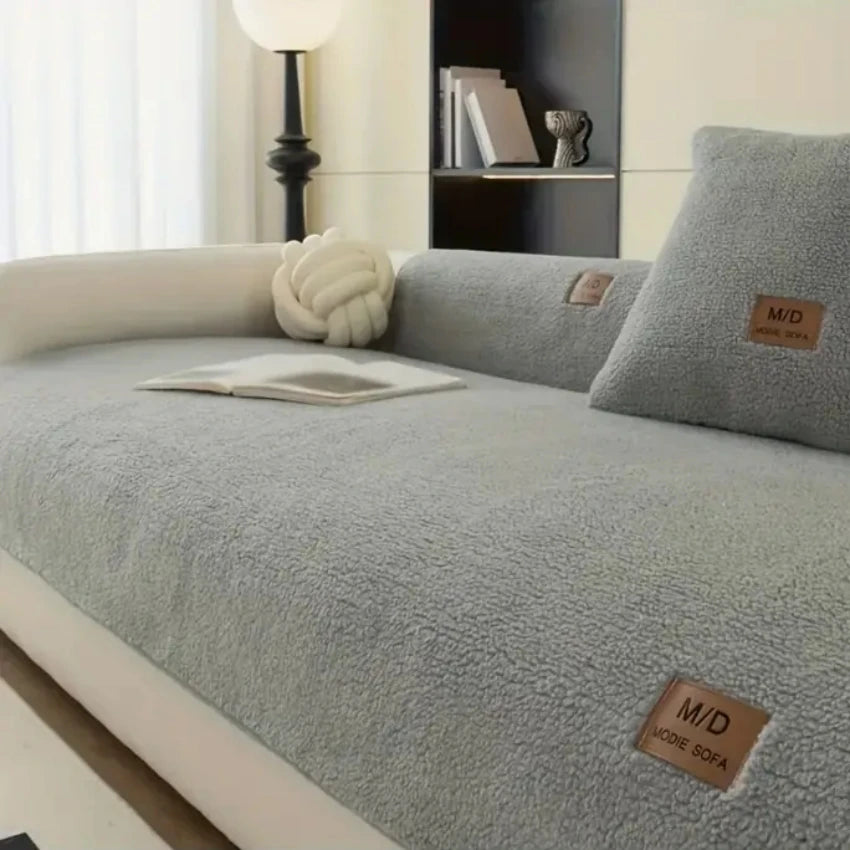 Housse de canapé sherpa gris clair avec une balle décorative blanche et une étiquette marron.