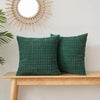 Two dark green corduroy pillows with a ribbed texture displayed on a wooden shelf next to a sunburst mirror.