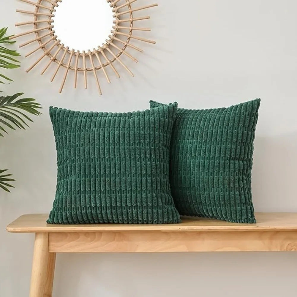 Two dark green corduroy pillows with a ribbed texture displayed on a wooden shelf next to a sunburst mirror.