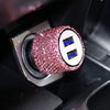 A close-up of a pink rhinestone dual USB car charger with blue accents inside a black device slot.