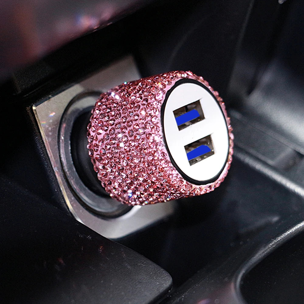 A close-up of a pink rhinestone dual USB car charger with blue accents inside a black device slot.