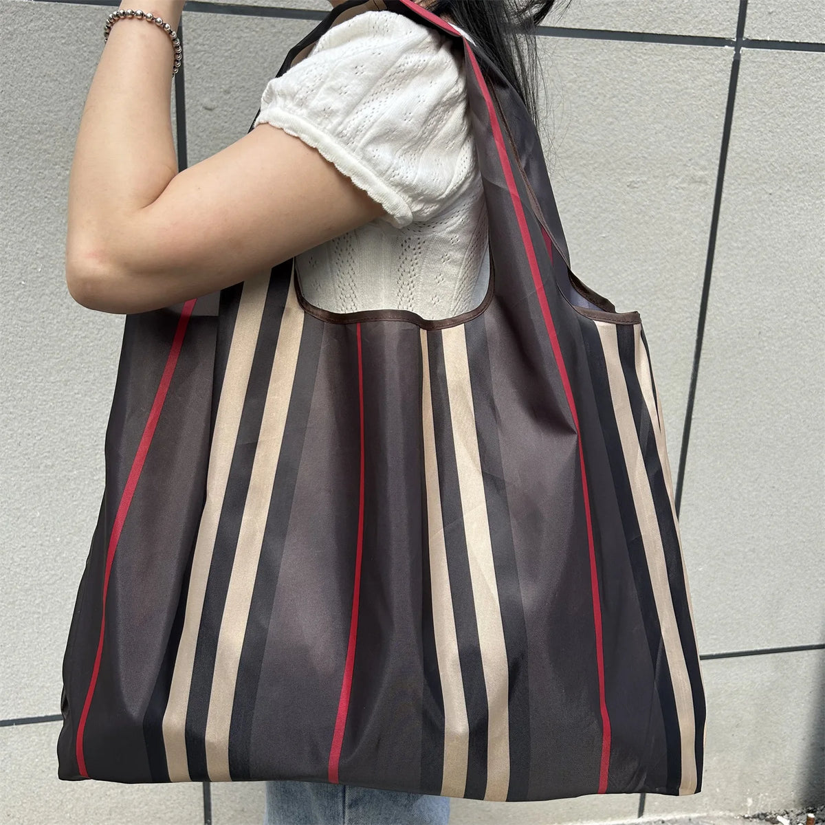 A person carrying a brown and beige striped foldable oxford cloth tote bag.