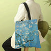 A light blue canvas tote bag featuring a white blossom tree design, carried by a person in a white blazer.