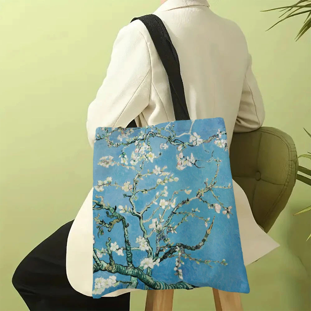 A light blue canvas tote bag featuring a white blossom tree design, carried by a person in a white blazer.