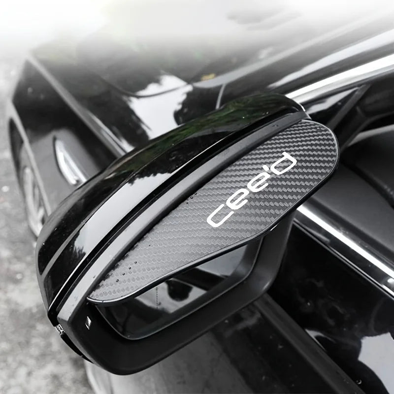 A close-up of a black carbon fiber rearview mirror rain guard installed on a car.