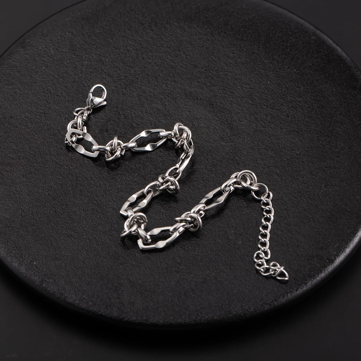 Silver titanium steel chain bracelet with knot detail lying on a black surface