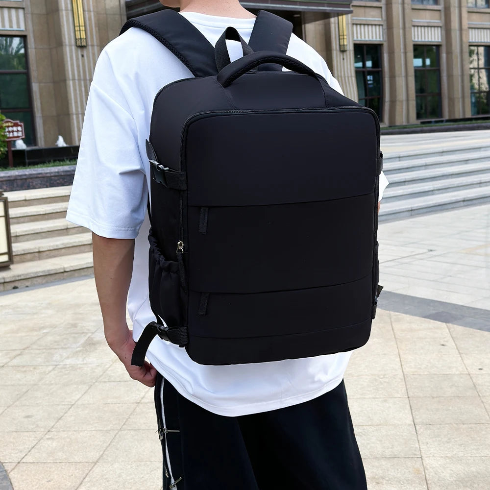 A black compact cabin travel backpack worn by a person standing outdoors.