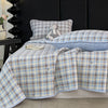 A plaid blue and beige quilted bedspread with a stuffed animal pillow on a dark background.