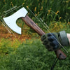 A hand-forged Viking tomahawk axe with a wooden handle and a green leather grip is shown outdoors.