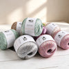 A collection of five skeins of MuYuan glitter yarn in various shades of green, pink, and silver resting on a white surface.