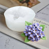 Un moule en silicone blanc rempli de cire est montré sur une page de cahier à côté d'une composition florale violette.