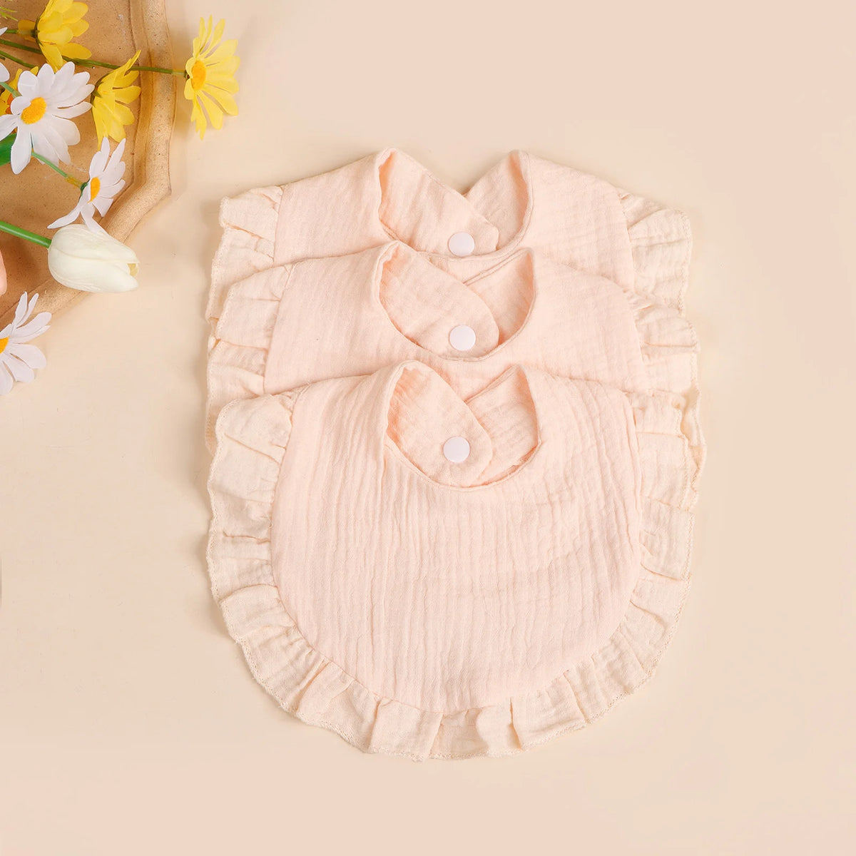 A light pink cotton ruffle bib is displayed on a neutral background with yellow flowers.