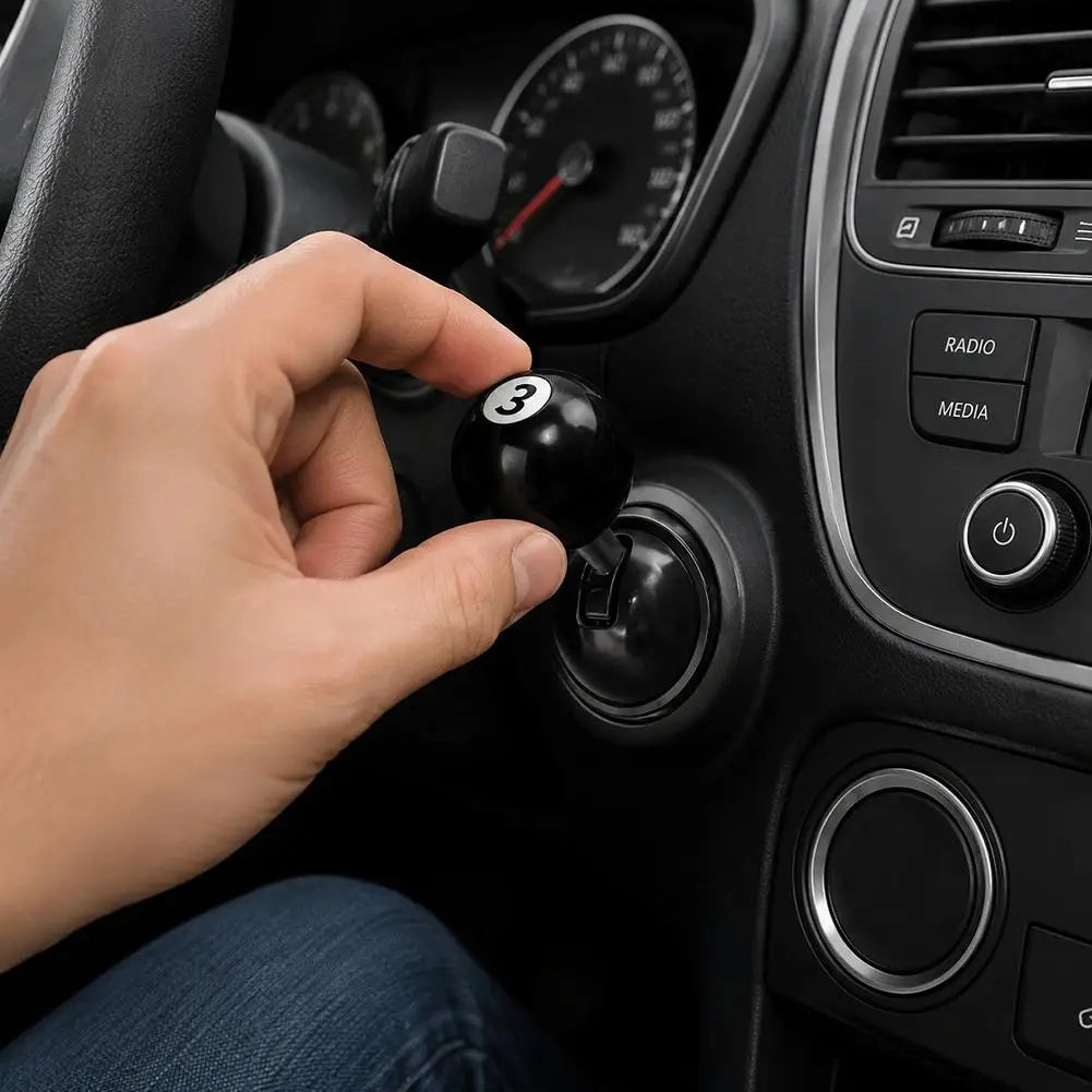 A hand is pressing a black metal push-to-start button cover with a billiard ball design on a car dashboard.