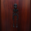 A dark, realistic sculpture of a human skeleton mounted on a wooden surface.