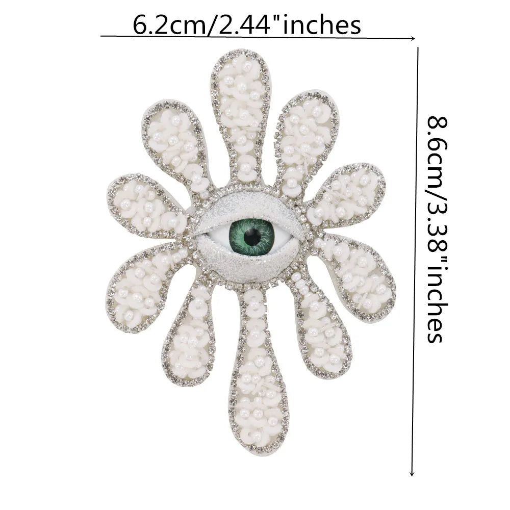 A sparkling beaded rhinestone eye patch with a green iris surrounded by white petals.