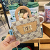 A hand holds a mini floral textured crossbody tote bag with light beige leather trim and gold chain details.