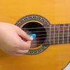 A hand is inserting a blue celluloid guitar pick into an adhesive holder on the soundboard of a yellow acoustic guitar.