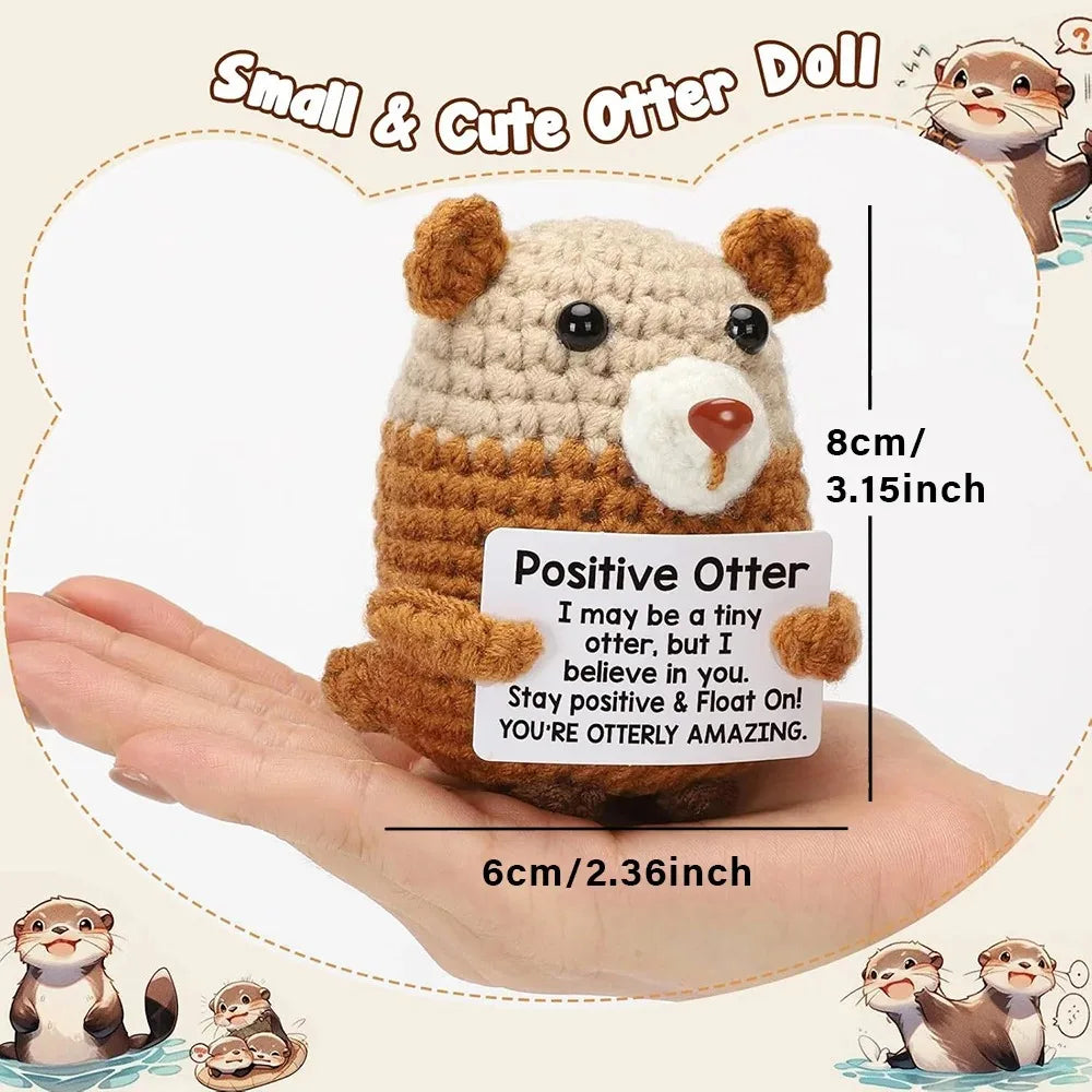 A handmade crochet positive otter doll in brown and white yarn is shown resting on a human hand.