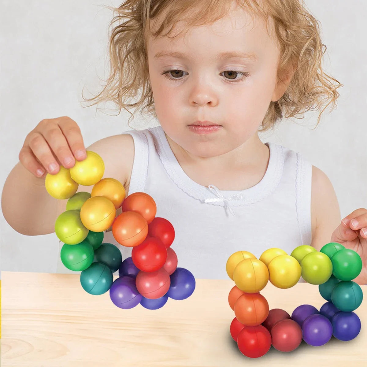 A young child is holding and arranging colorful 3D rotating fidget balls on a wooden surface.