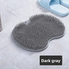 A dark gray suction cup foot massage mat with exfoliating bristles is shown on a light surface.