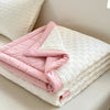 A folded pink and white waffle-weave summer quilt on a bed.