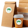 A brown paper bag and a disposable coffee cup both feature a green tea logo sticker.
