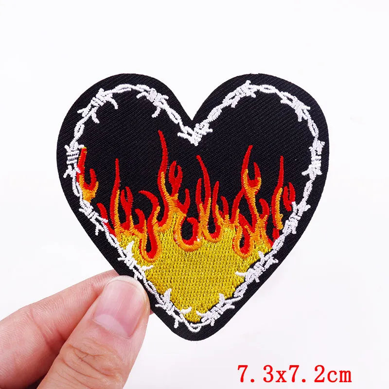 Black heart shaped patch embroidered with orange and yellow flames outlined in white thread