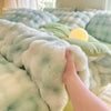 A hand touches a fluffy, light green and blue patterned fleece duvet cover with a yellow light bulb resting on the fabric.