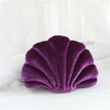 A deep purple velvet shell print throw pillow resting on white fabric.