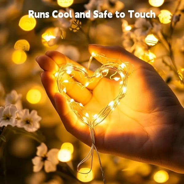 A hand holds a glowing heart-shaped string of LED fairy lights surrounded by soft, warm bokeh lights.