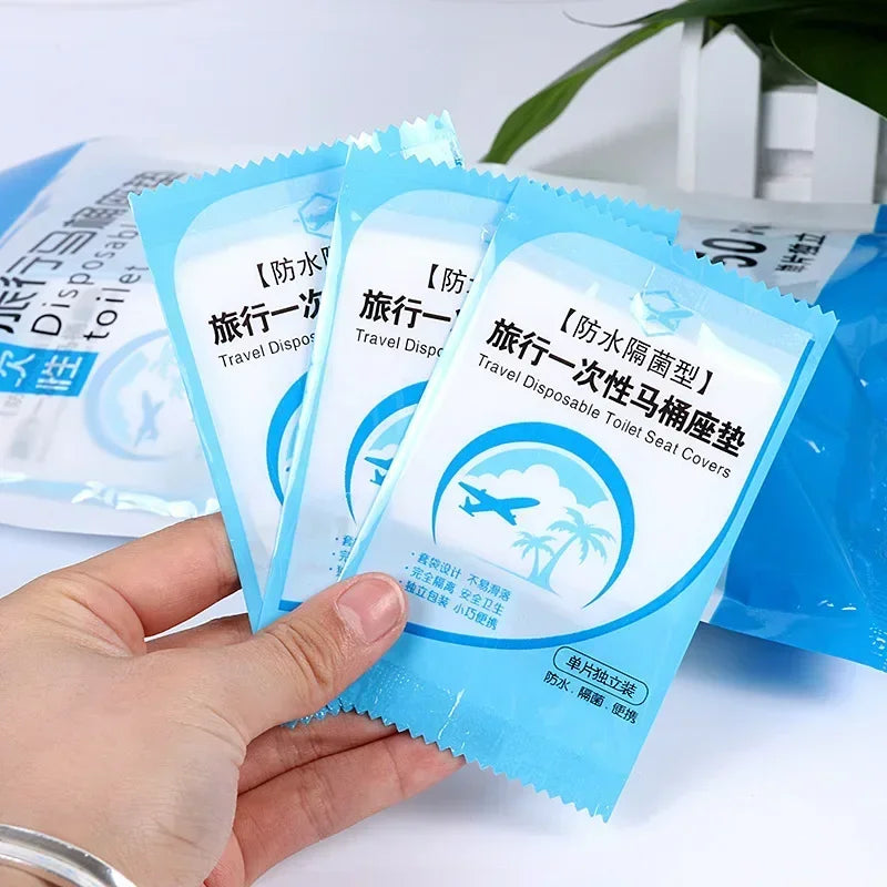 A hand holds a pack of disposable toilet seat covers designed for travel and waterproof use.
