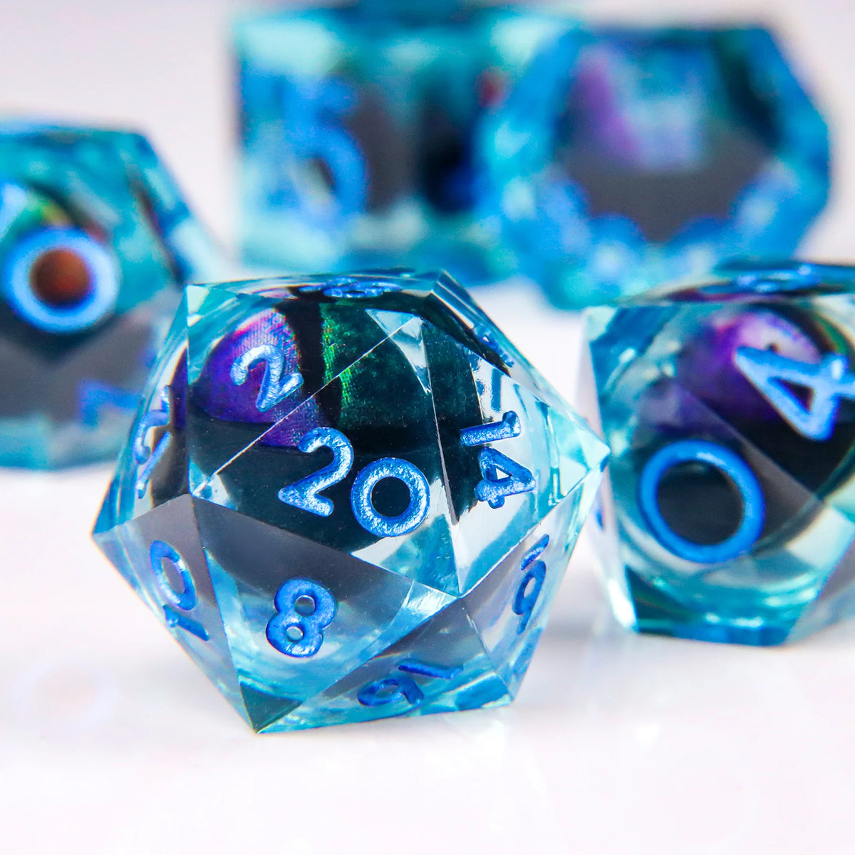 A close-up of a translucent blue liquid core resin die with a dragon eye design, resting on a white surface.