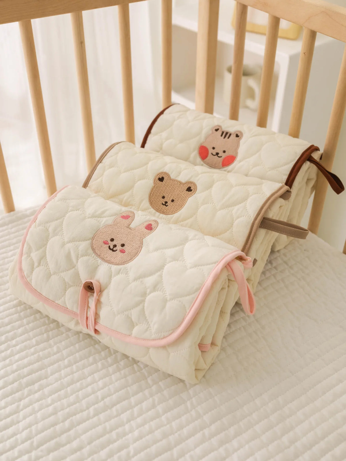 A cream quilted foldable portable diaper changing pad with cute animal embroidery resting on a light surface.