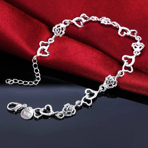 A sterling silver heart and flower chain bracelet displayed on a dark surface against a red fabric background.