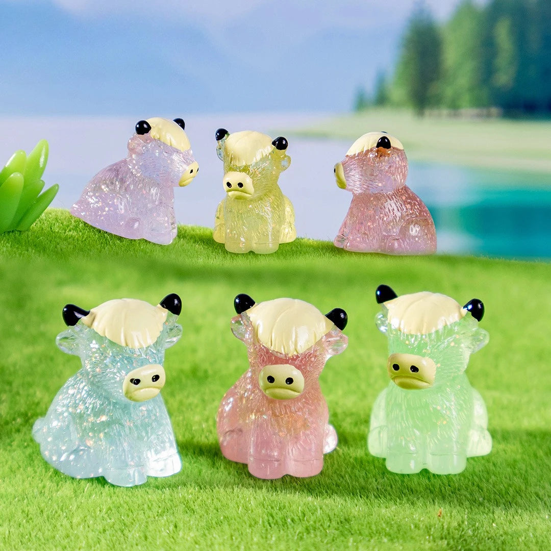 A set of four adorable resin highland cow figurines in various shades of pink and yellow sitting on green grass.
