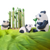 Wooden animal figures of a panda and a bear sitting among green bamboo stalks on a green fabric background