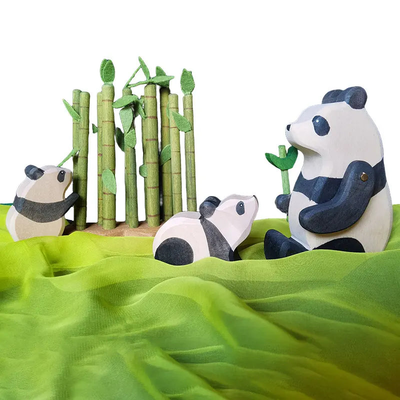 Wooden animal figures of a panda and a bear sitting among green bamboo stalks on a green fabric background