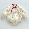 A cream-colored baby girl floral lace cotton romper with red trim and buttons.