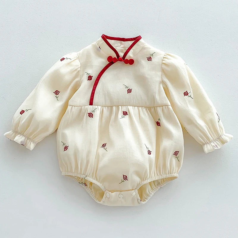 A cream-colored baby girl floral lace cotton romper with red trim and buttons.